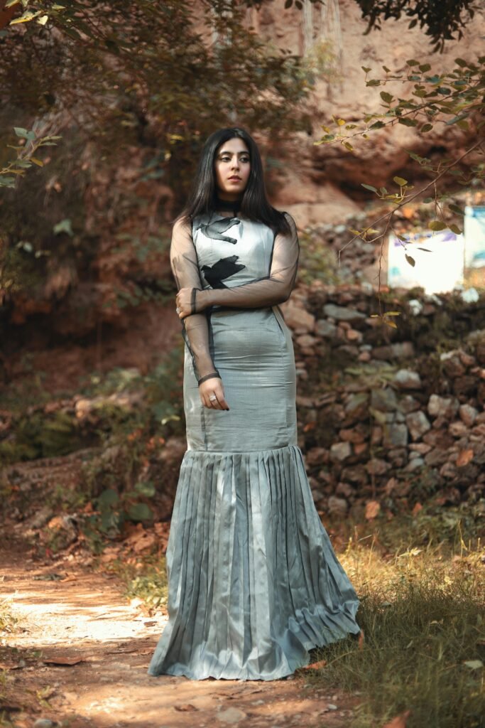 Fashion model in a flowy silver dress posing outdoors in natural light.