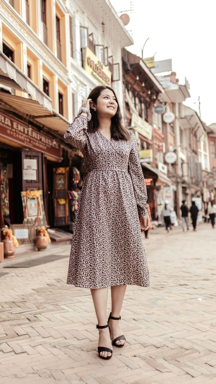A stylish woman in a floral dress smiles while walking on a bustling city street.